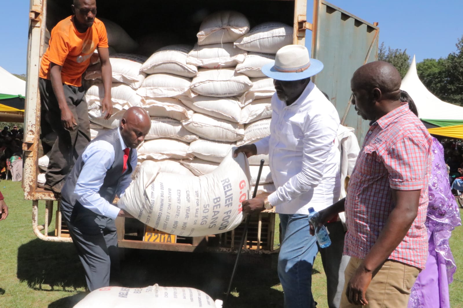 Public Service, Human Capital Development and Special Programmes CS Geoffrey Ruku (R) carries relief food with (L) Kangundo MP Fabian Kyule next to a truck full of relief food that will be distributed to public schools in the region